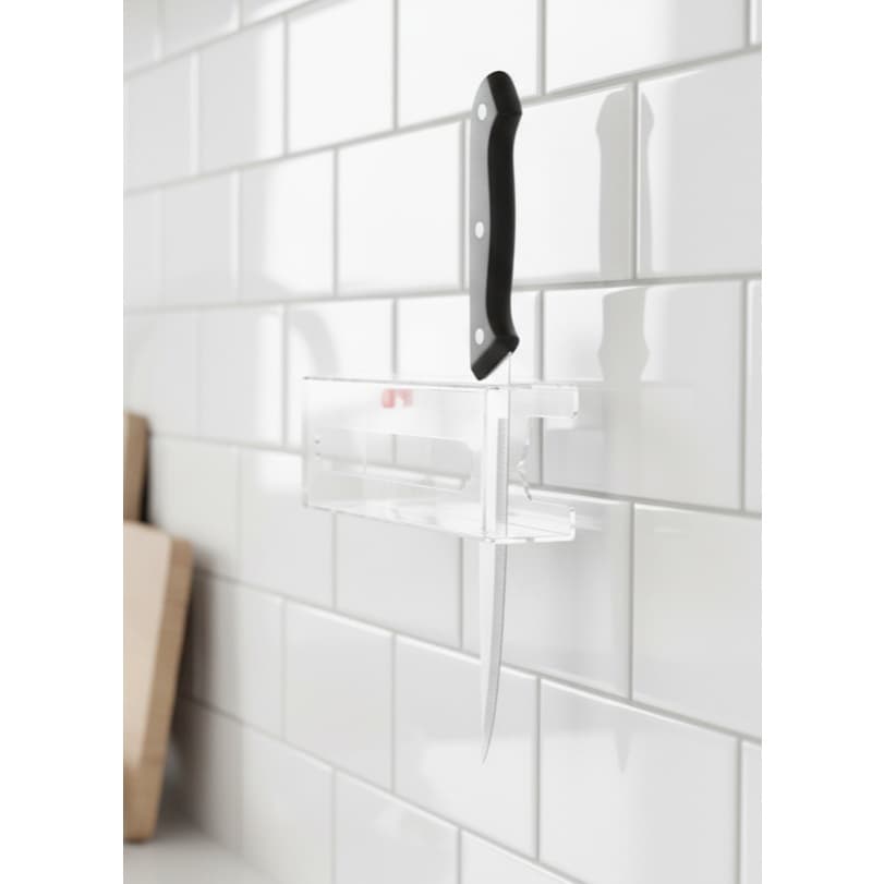 Suporte de faca acrílico transparente com cinco furos, fixado em uma parede de azulejos brancos.