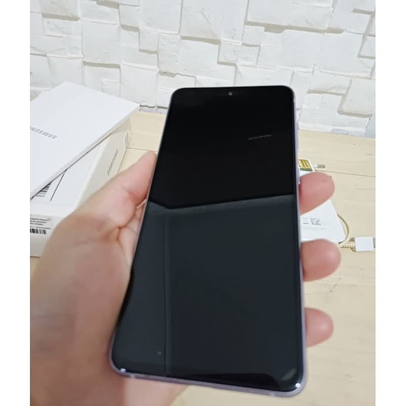 Samsung Galaxy S21 Fe preto, segurado na mão, com caixas originais ao fundo