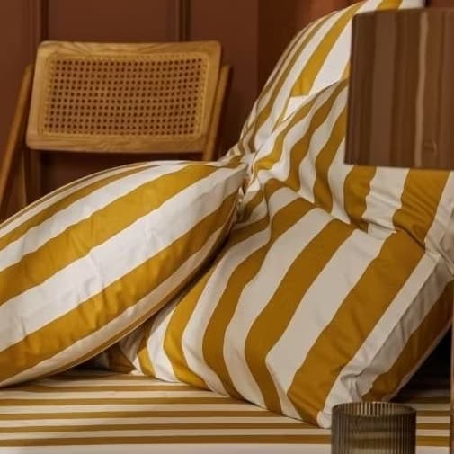 Edredom listrado amarelo e branco em uma cama com almofada e cadeira de vime