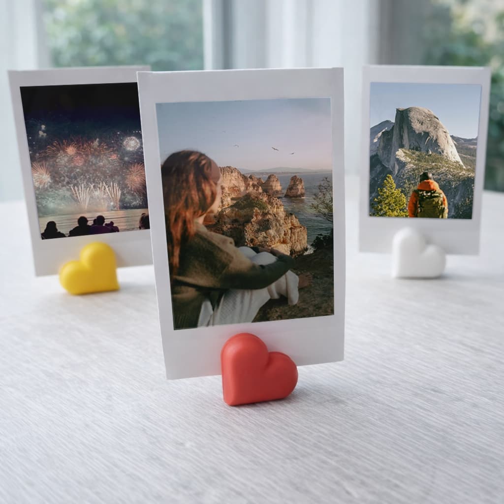 Três suportes de fotos em formato de coração para Polaroid com imagens de paisagem, mulher e fogos de artifício.