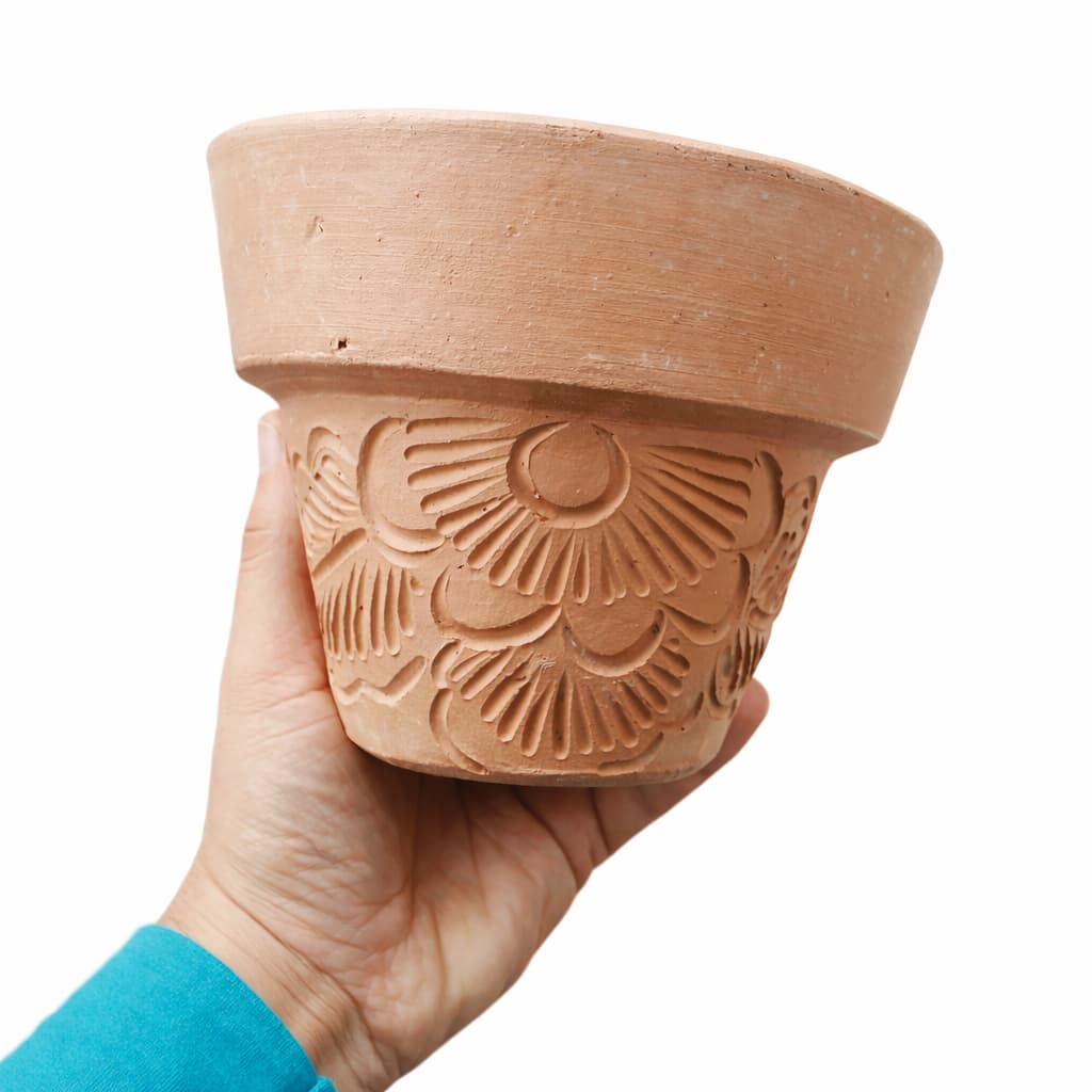 Mão segurando vaso de barro marrom com padrão floral esculpido