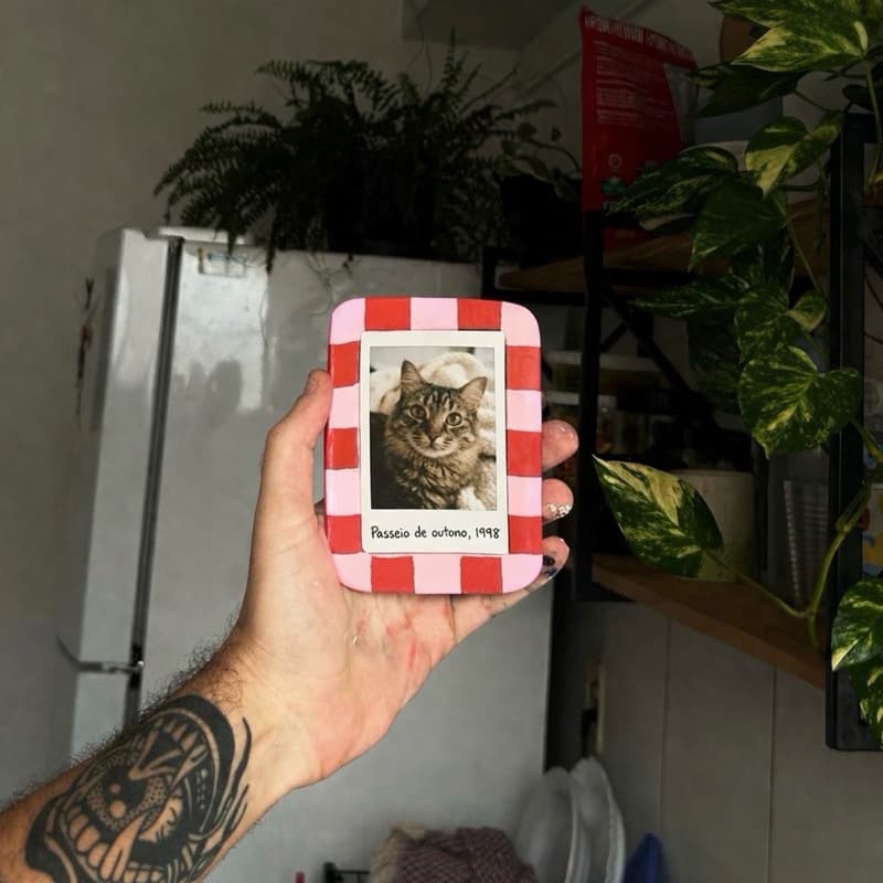 Porta retrato quadrado com borda xadrez vermelha e branca, contendo uma foto de um gato.