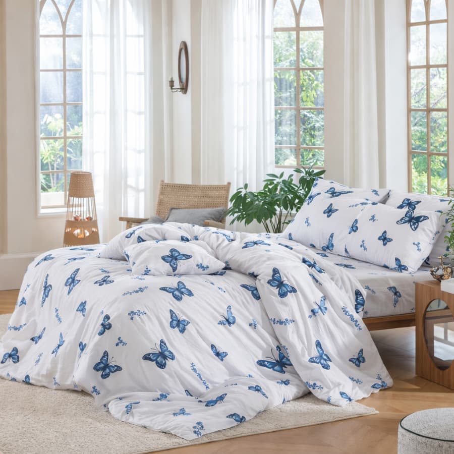 Quarto com cama de casal e edredom com estampa de borboletas azuis.
