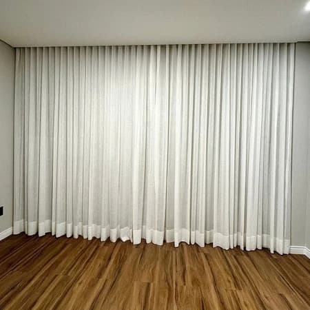 Cortina branca com trilho suíço duplo e forro blackout em uma parede cinza com fundo de madeira escura