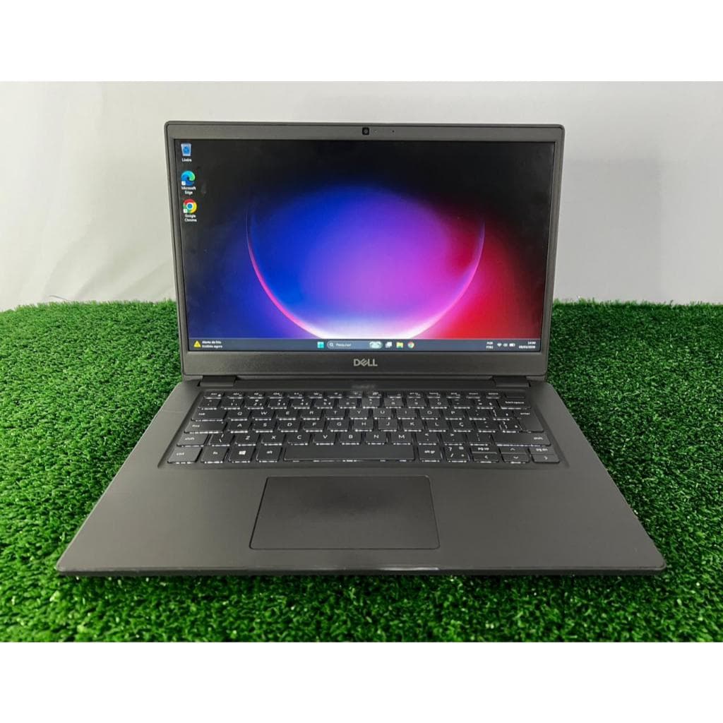 Notebook Dell Latitude 3410 aberto sobre grama verde, mostrando a tela de inicialização do Windows.
