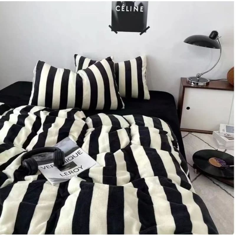 Edredom listrado preto e branco sobre cama de casal com almofadas combinando, lampião e headphone pretos.