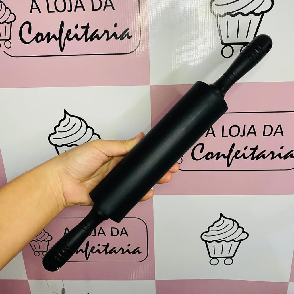 Rolo abridor de massa preto em silicone antiaderente para pizza, pão e macarrão, segurado na mão contra fundo de cupcakes