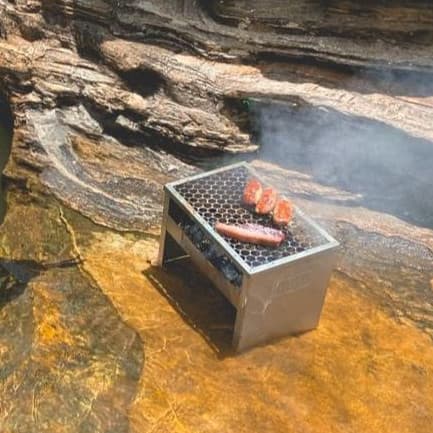 Churrasqueira portátil pequena galvanizada dobrável a carvão grelhando carnes em cenário natural