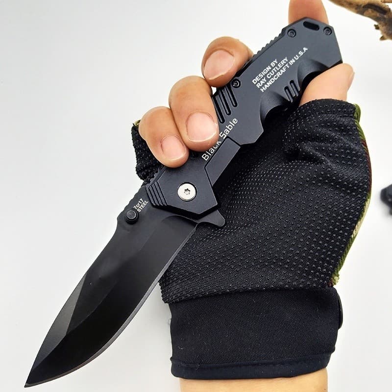 Canivete preto com lâmina curva e cabo texturizado, segurado por mão com luvas pretas, design Ray Cutlery.