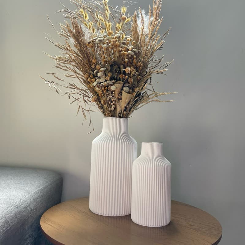 Dois vasos decorativos brancos com flores secas em uma mesa de madeira