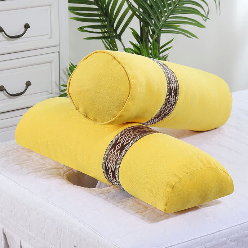 Almofadas cilíndricas amarelas com estampas marrons sobre cama branca