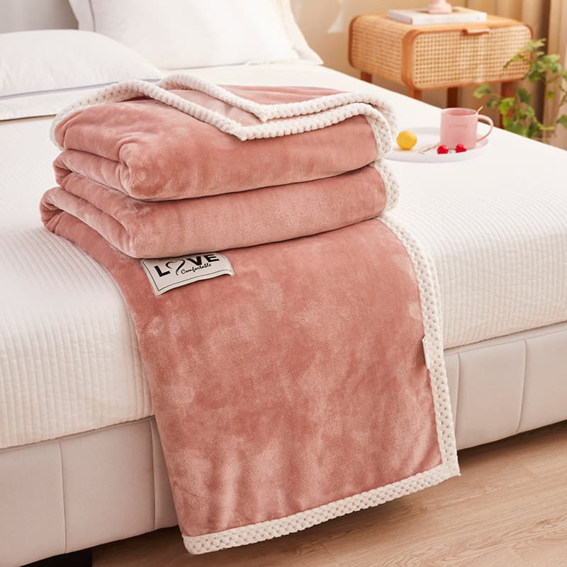 Três cobertores rosa de lã coral empilhados em uma cama branca com a marca LOVE visível