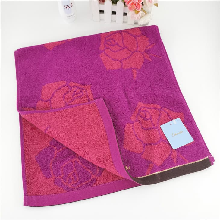 Toalha de banho rosa com estampa floral de rosas, borda marrom e rótulo azul