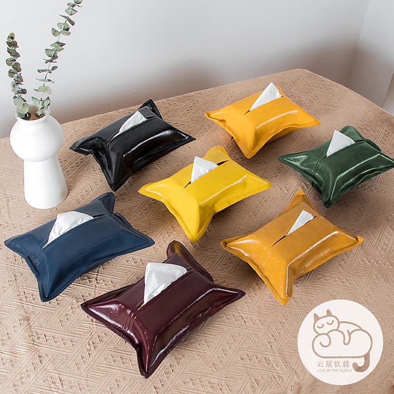 Porta-lenços de tecido de couro em várias cores, dispostos em uma superfície com um vaso branco e planta verde.