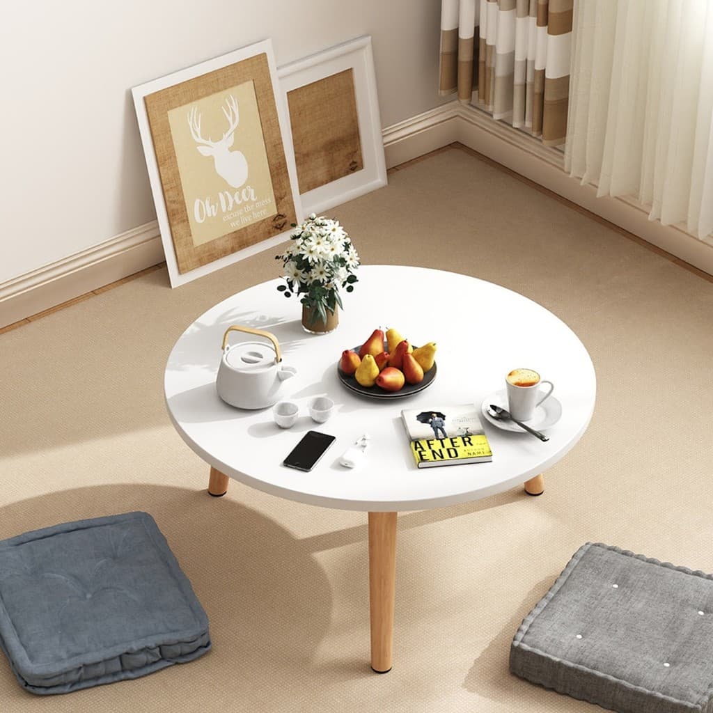 Mesa redonda branca estilo minimalista com frutas, café e livro no centro da sala.