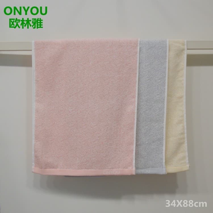 Três toalhas de fibra de bambu penduradas em um suporte metálico, cores rosa, cinza e bege.