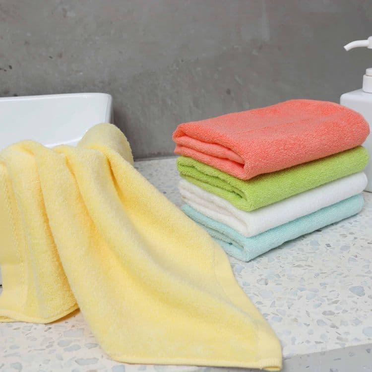 Toalhas de fibra de bambu em cores amarela, verde, laranja e azul claro empilhadas em um balcão