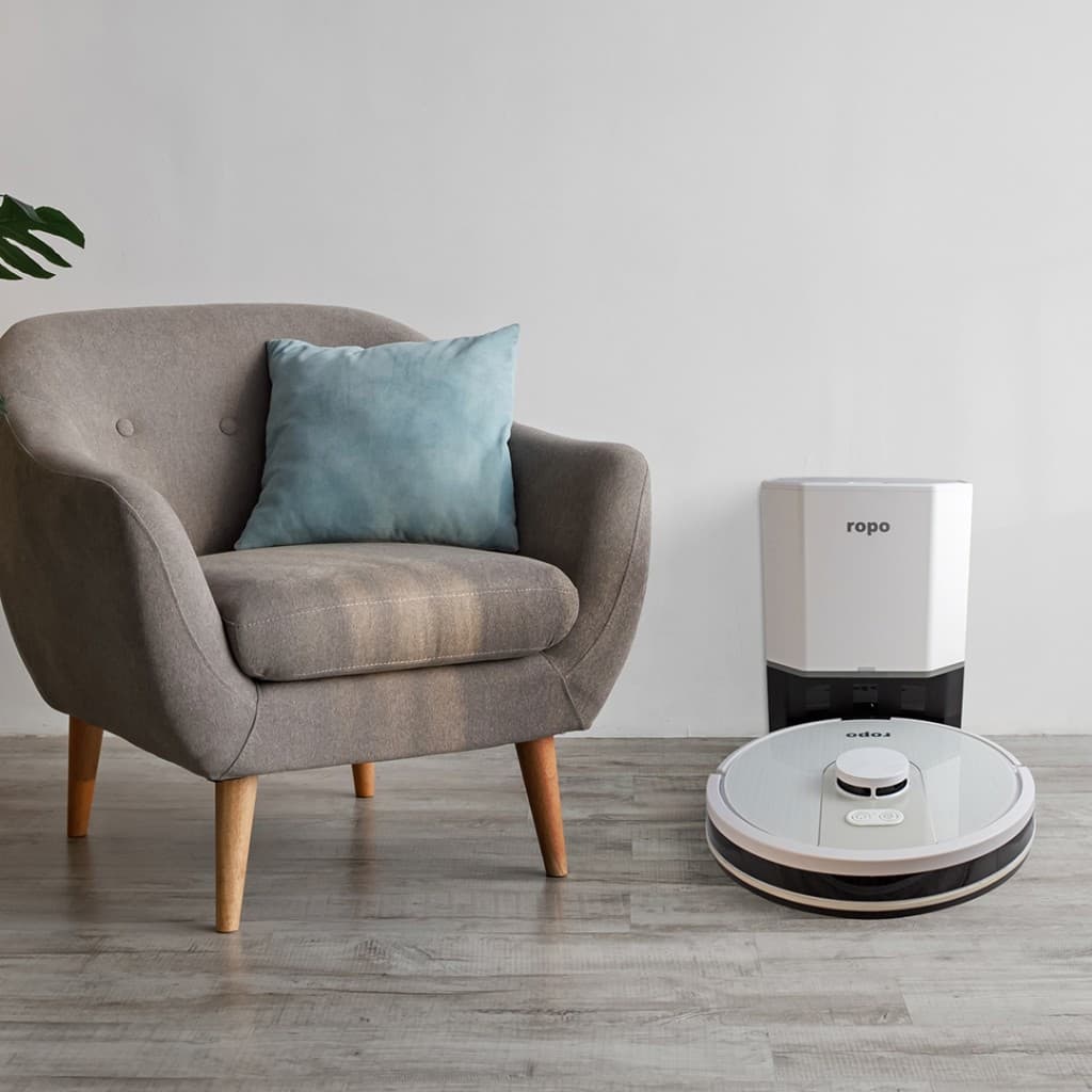 Robô aspirador Ropo Glass 4 Pro em um ambiente limpo com uma cadeira cinza e parede branca