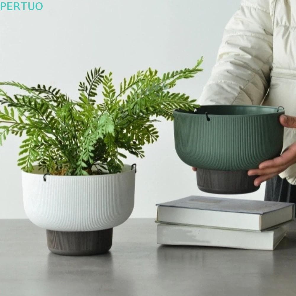 Vasos suspensos verde e branco de PERTUO com planta verde, segurados por uma pessoa, com livros ao fundo.