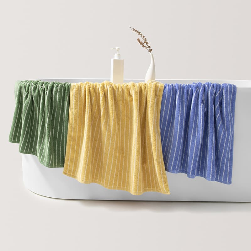 Toalhas de banho adultas listradas de algodão puro em verde, amarelo e azul penduradas em uma banheira branca