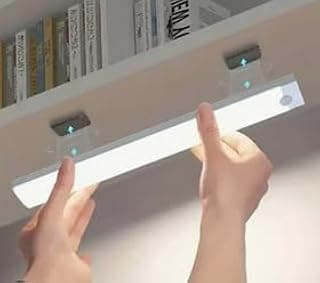 Luminária LED recarregável USB branca em uma prateleira acima de livros, com luz brilhante e controles na parte inferior.