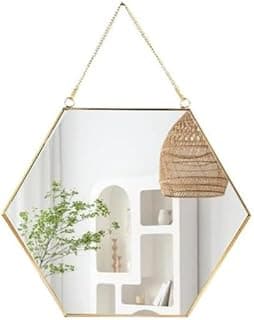 Espelho hexagonal de parede com moldura dourada e corrente, refletindo planta e luminária.