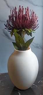 Vaso decorativo oval branco com flor vermelha artificial, sobre superfície de mármore cinza, fundo azul claro.