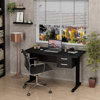 Mesa de escritório preta com gaveteiro e pés de metal, monitor aberto, lâmpada, cadeira e vaso de planta.