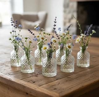 Sete mini vasos de vidro com flores silvestres em uma mesa de madeira