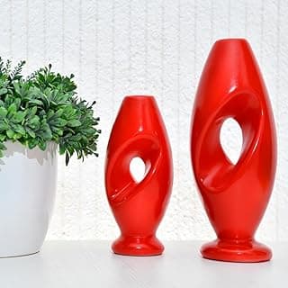 Dois vasos decorativos vermelhos modernos com furos centrais, ao lado de um vaso branco com planta verde.