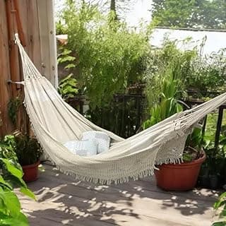 Rede de dormir branca com almofadas, varanda com plantas e muro de madeira