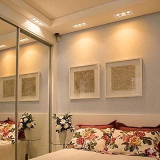 Quarto com cama e decoração floral, três quadros na parede, iluminação decorativa.
