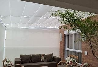 Cortina rolo branca (off-white) em área externa com sofá marrom e parede de tijolos