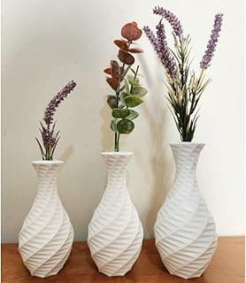 Kit com 3 vasos decorativos brancos com plantas artificiais, estilo ondas, sobre uma mesa de madeira.
