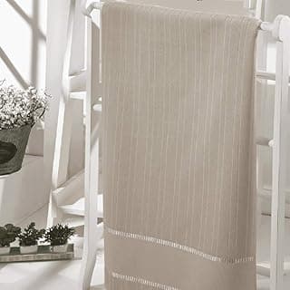 Toalha de banho lisa bege pendurada em suporte branco, com borda decorativa.