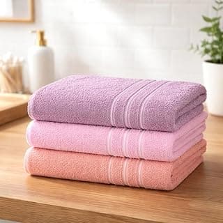 Três toalhas de banho Teka em cores rosa, rose e vinho empilhadas sobre uma superfície de madeira.