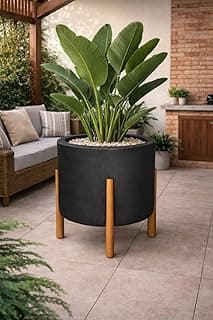 Vaso grande preto com pés de madeira para plantas modernas em polietileno, terraço com piso de concreto e plantas verdes.