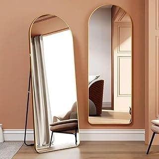 Espelho oval de chão com moldura dourada refletindo uma sala com cadeira e porta