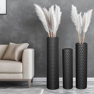 Vasos altos pretos decorativos de metal com pampas brancas em um ambiente minimalista.