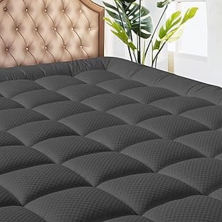 Capa de colchão queen size cinza escuro sobre colchão, com cabeceira estofada e planta ao fundo.