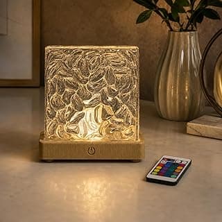 Luminária LED RGB em forma de cubo com controle remoto, efeito projetado de luz ambiente, base de madeira, design em acrílico texturizado, iluminação multicor, mesa com planta e moldura no fundo.
