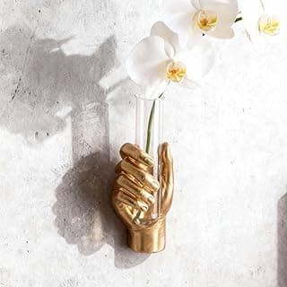 Escultura de parede dourada com vaso de flores brancas