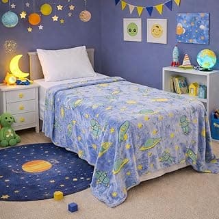 Manta infantil luminescente com estampa de astronauta e planetas, cobrindo cama infantil, fundo azul com decoração espacial.