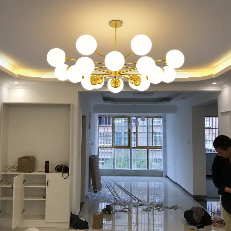 Lustre moderno de LED com esferas de vidro e estrutura dourada em sala com piso de mármore e grandes janelas.