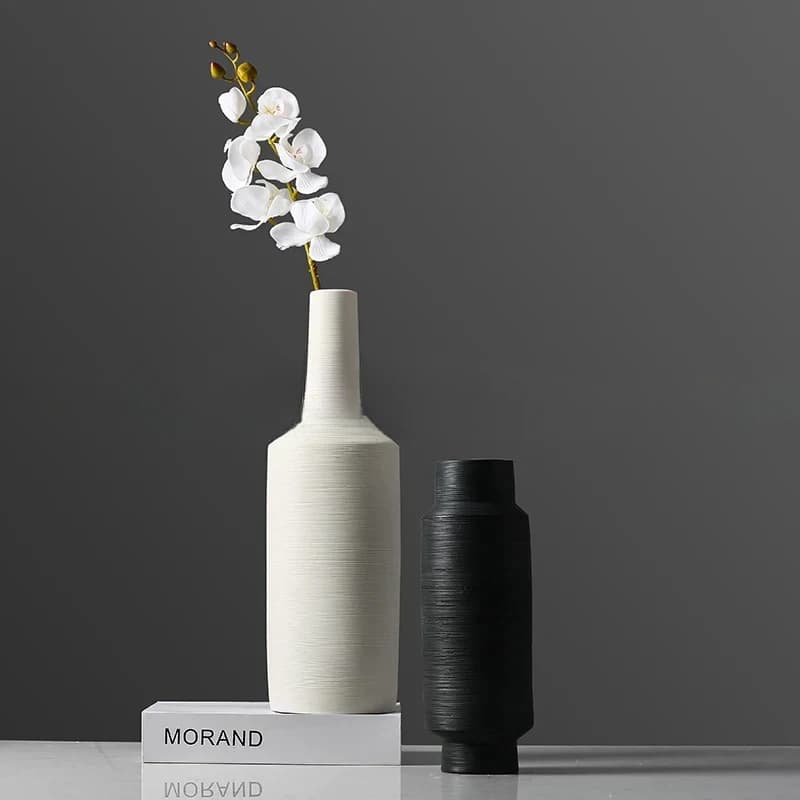 Vasos decorativos de cerâmica branco e preto com flor branca sobre livros