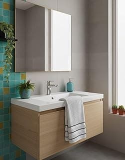 Banheiro com lavabo de cor bege, azulejos azuis e amarelos, pia com tanque duplo, espelho e toalha branca com listras pretas.