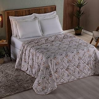 Edredom solteiro floral rosa e branco, cama com roupa de cama branca, fundo cinza e cadeira de madeira.